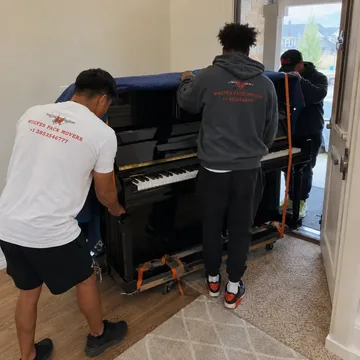 Piano movers guiding a piano through a narrow doorway in a Portland home