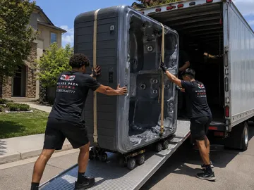 Crew pushing a hot tub on its side up a truck ramp — hot tub delivery serving Seattle